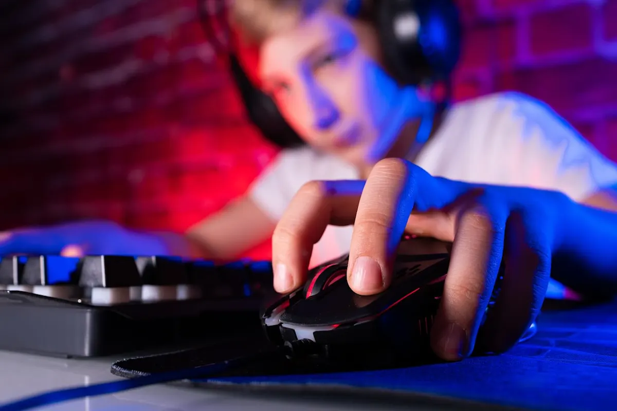 Junger Gamer mit Kopfhörern sitzt in einem Gaming-Room und hat die Finger seiner linken Hand auf einer Gamingmaus.