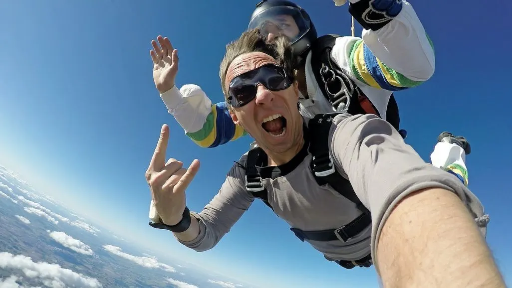 Zwei Personen beim Fallschirmsprung in luftiger Höhe über den Wolken.