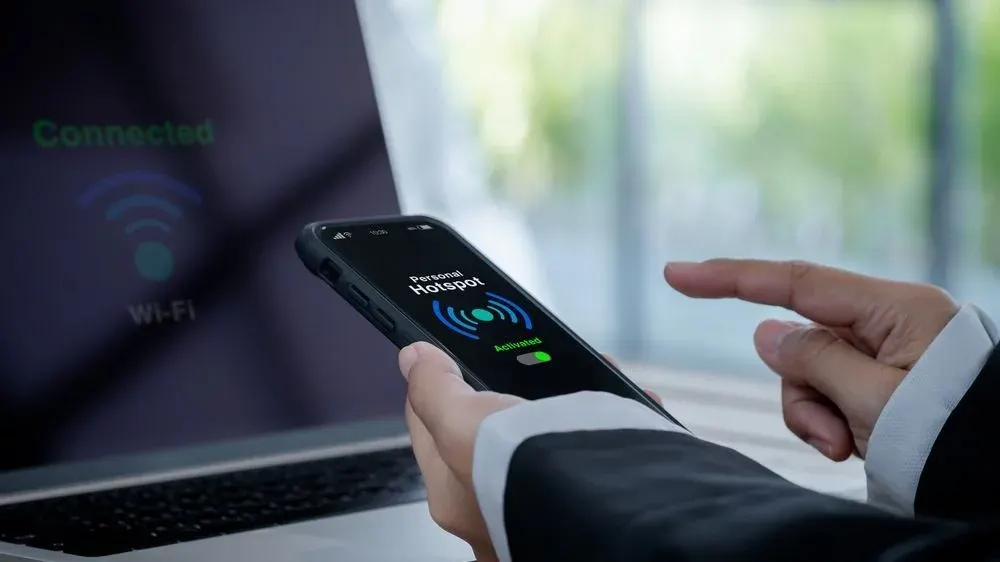 Person hält Handy mit Wlan symbol for einem Laptop der auch ein Wlan Symbol zeigt