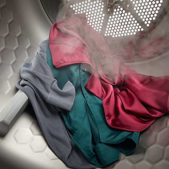 Ein Wäschetrockner mit grauer, grüner und roter Kleidung im Inneren und etwas Dampf.