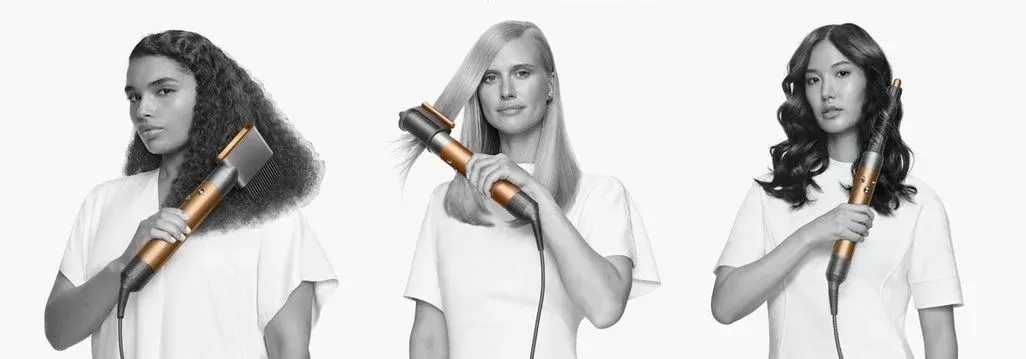 Drei Frauen mit unterschiedlichen Haartypen und Frisuren halten Dyson Haarstyler mit goldenem Heizelement in der Hand – lockiges Haar, glattes Haar und welliges Haar vor weißem Hintergrund.