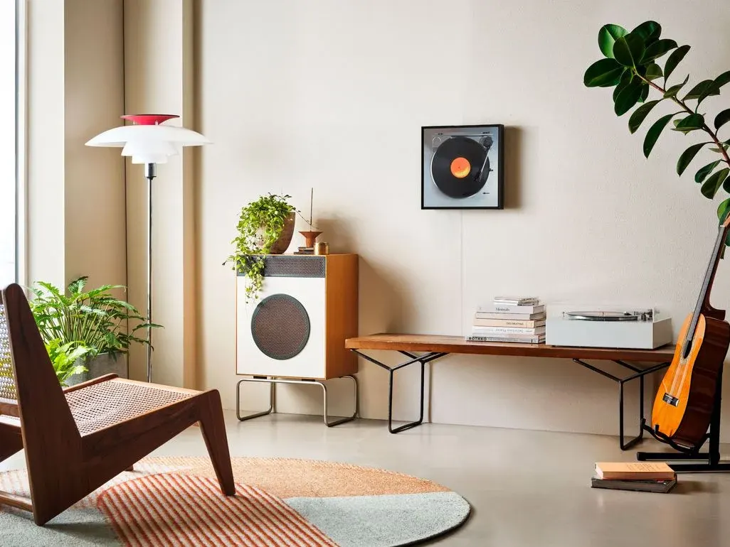 Modern eingerichtetes Wohnzimmer mit Holzstuhl, Pflanzen, Sideboard und Bank; an der Wand hängt ein quadratischer Samsung Music Frame im Look eines Plattenspielers und fügt sich dezent als Designobjekt ins Interieur ein.