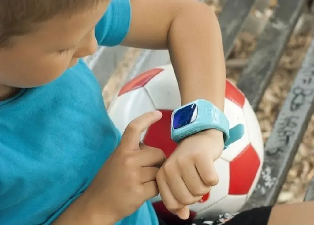 Kind sitzt auf einer Bank mit einem Fußball unter dem Arm und tippt auf eine Smartwatch