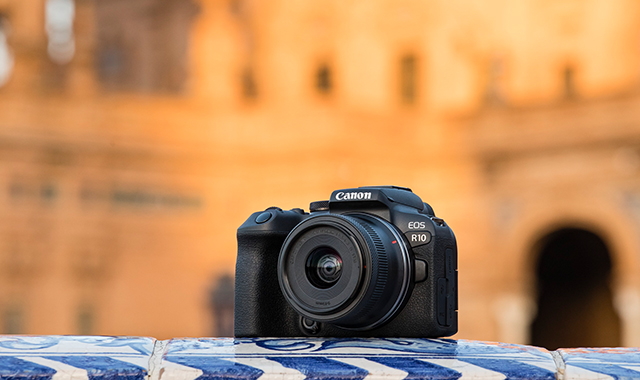 Eine schwarze Canon EOS R10 Kamera liegt auf blau-weiß gemusterten Fliesen. Im Hintergrund ist ein beiges Gebäude zu sehen.