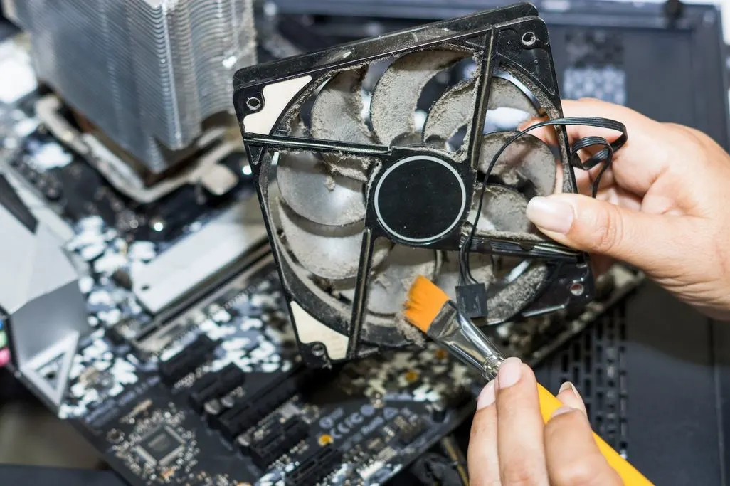 Stark verstaubter Computer-Lüfter wird mit Pinsel gesäubert.