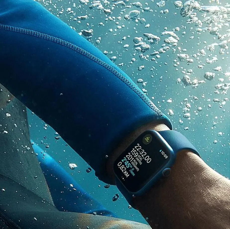 Apple Watch an einem Arm unter Wasser mit blauem Neoprenanzug.