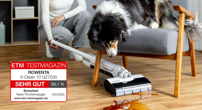  Person saugt Flüssigkeit auf dem Holzboden mit dem Rowenta X‑Clean 10 Nass-Trockensauger, Hund schaut vom Sessel zu, ETM-Testmagazin-Siegel „Sehr gut“.