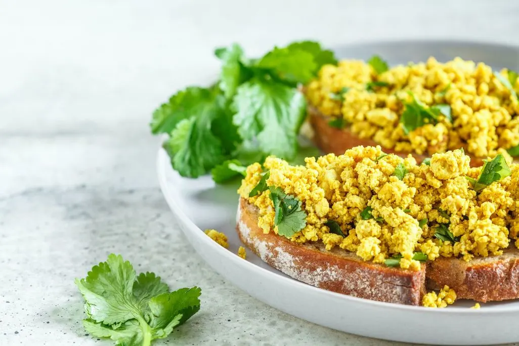 Zwei Scheiben Brot mit veganem Rührei und frischem Koriander.