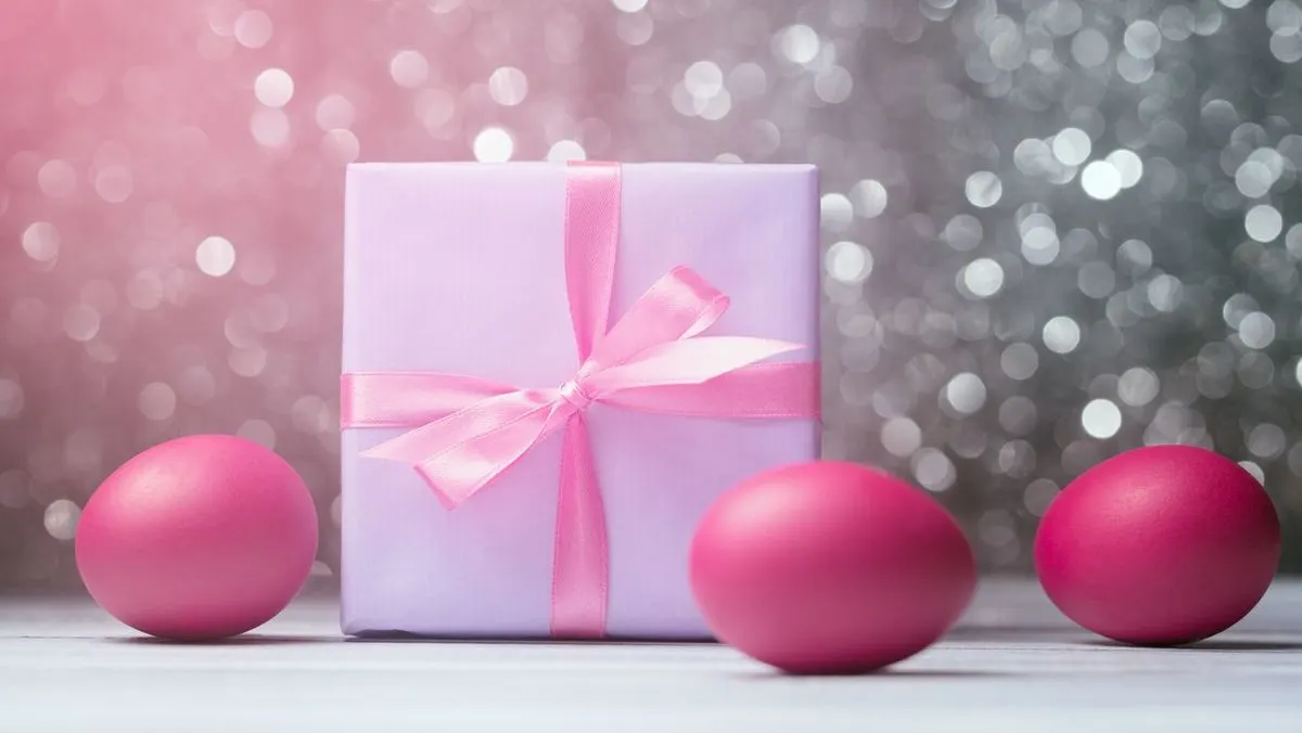 Ein rosa Geschenk mit Schleife steht zwischen drei pink gefaäbten Ostereiern vor glitzerndem Hintergrund.