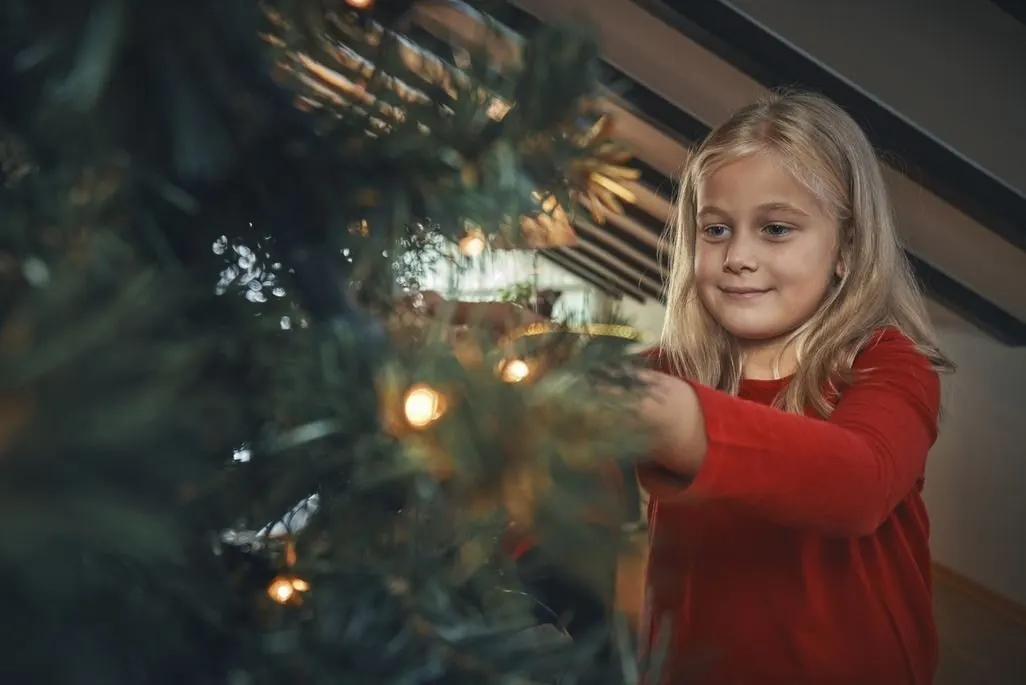 Kind in rotem Pullover schmueckt einen Weihnachtsbaum mit Lichtern