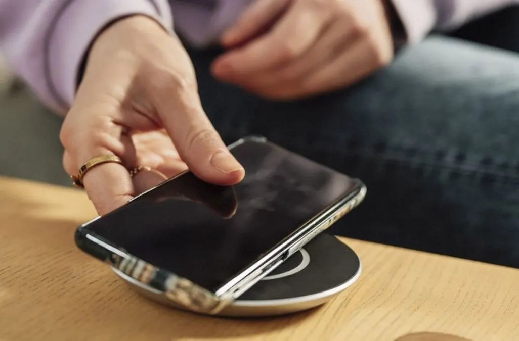 Hand legt Smartphone auf eine kabellose Ladestation auf einem Holztisch.