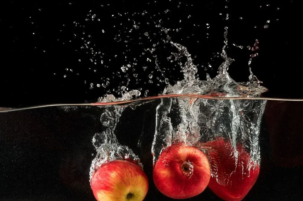Drei rot-gelbe Äpfel tauchen ins Wasser ein, erzeugen Spritzer und Wellen vor schwarzem Hintergrund.