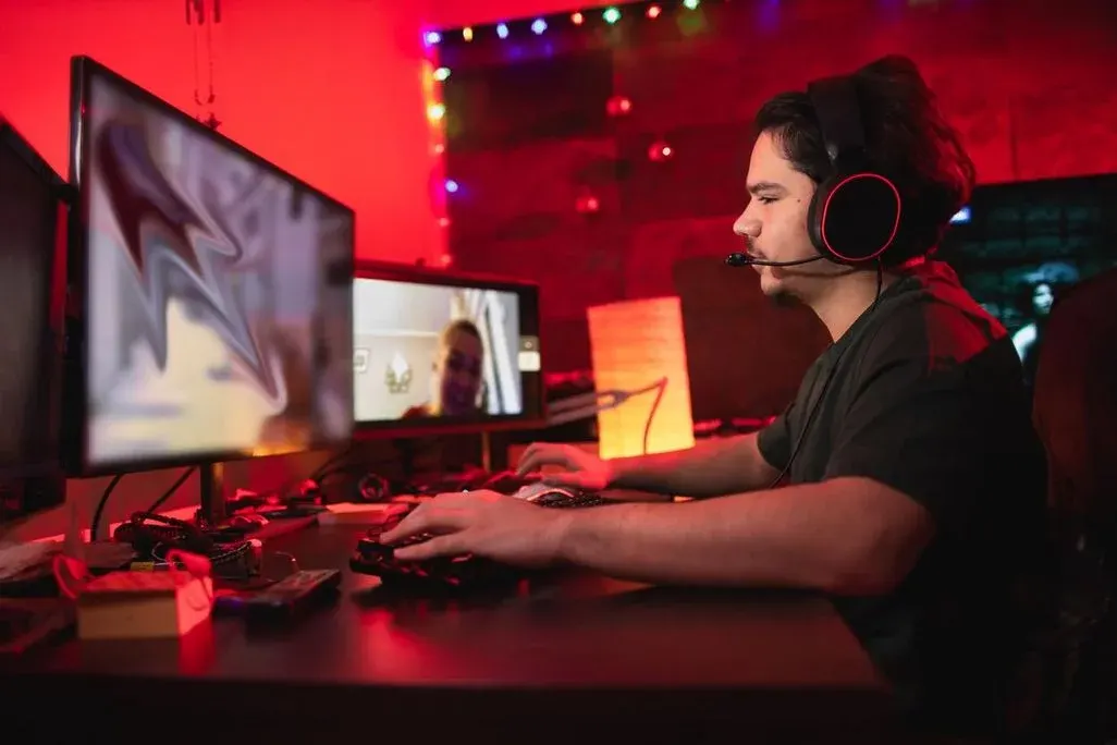 Wir betrachten seitlich einen jungen Mann, der mit Headset in einem Gaming-Zimmer auf einen Monitor blickt und spielt.