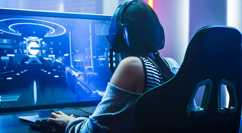 Eine Person sitzt auf einem Gaming-Stuhl vor einem Monitor, auf dem ein blaues Videospiel zu sehen ist.