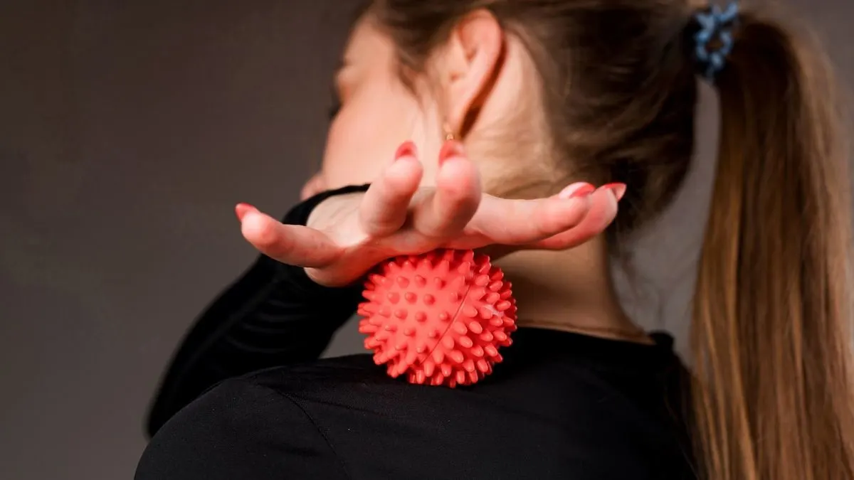 Eine Frau massiert ihren Nacken mit einem roten Igelball.