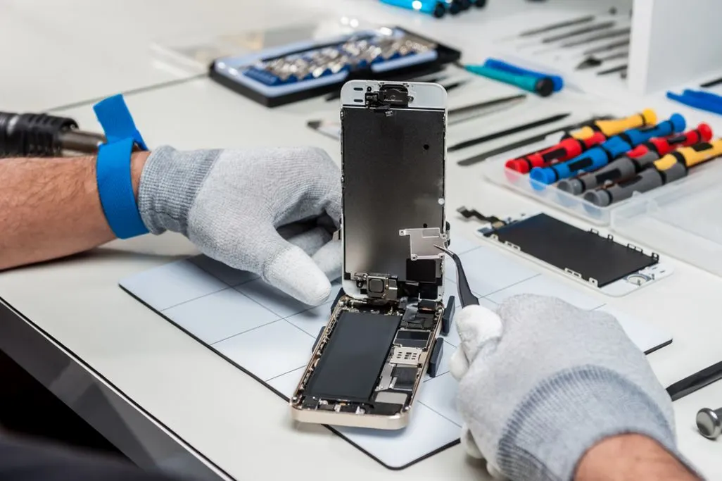 Techniker mit Handschuhen repariert ein geöffnetes Smartphone auf einer Werkbank.