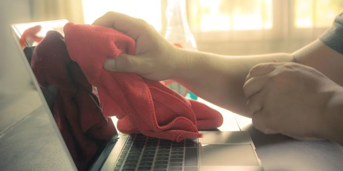 Hand reinigt Laptop-Bildschirm mit rotem Mikrofasertuch bei warmem Sonnenlicht.