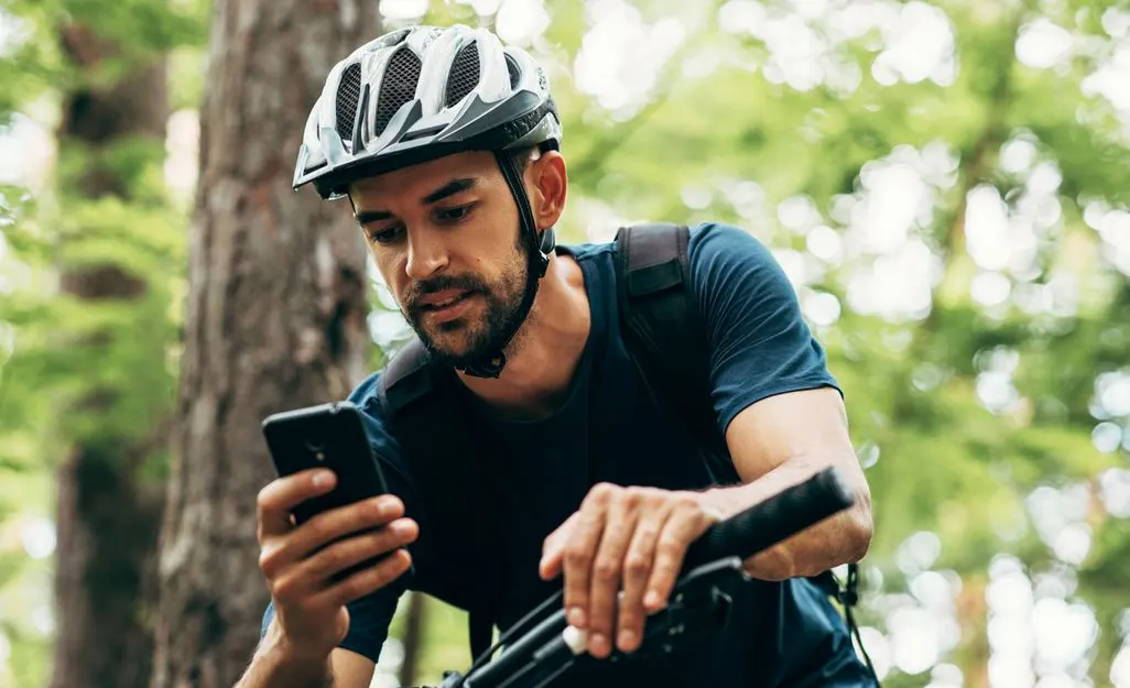 Person mit Fahrradhelm benutzt Smartphone im Wald