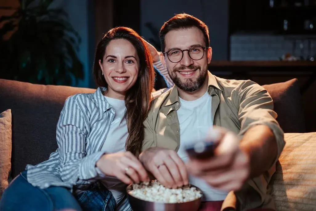 Ein Mann und eine Frau sitzen auf dem Sofa mit Popcorn, er hält eine Fernbedienung in der Hand