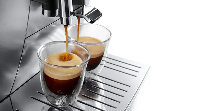 Zwei klare Gläser füllen sich mit braunem Kaffee aus einer silbernen Kaffeemaschine auf einer silbernen Abtropffläche.