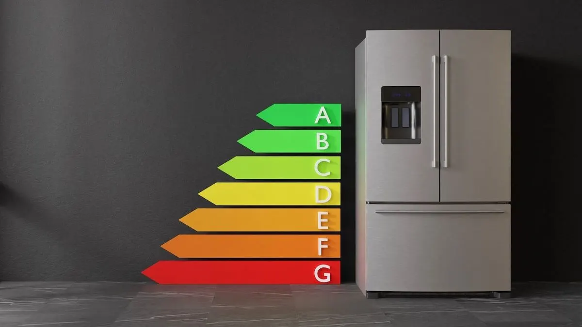 Edelstahlkühlschrank mit Wasserspender neben Energieeffizienz-Skala von A (grün) bis G (rot) vor dunkler Wand und Boden.