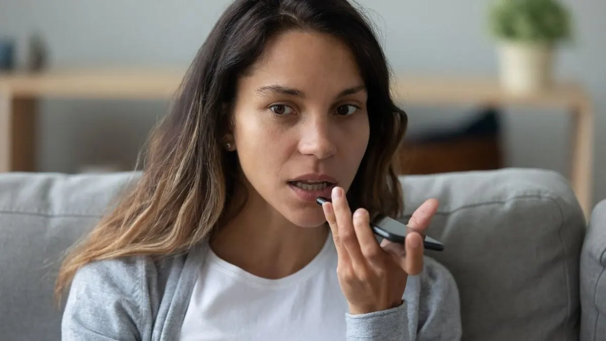 Eine Frau sitzt auf einem Sofa und spricht in ein Smartphone.
