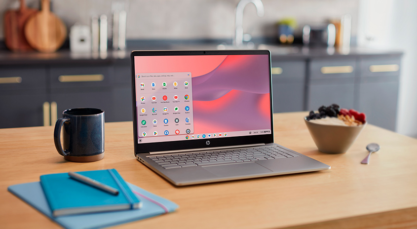 Auf einem Tisch steht ein geöffneter Laptop, daneben eine Tasse, ein Notizbuch, eine Schüssel mit Beeren und ein Löffel.