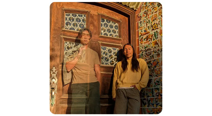Zwei Personen vor einer verzierten Holztür und einer Wand mit bunten Fliesenmustern.