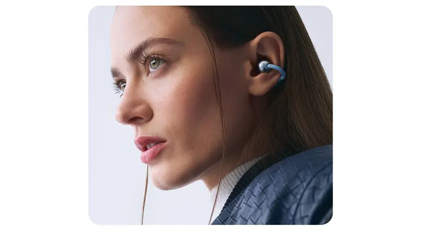 Nahaufnahme einer Person im Profil mit im Ohr sitzenden, blauen In‑Ear-Kopfhörern, vor hellem Hintergrund.