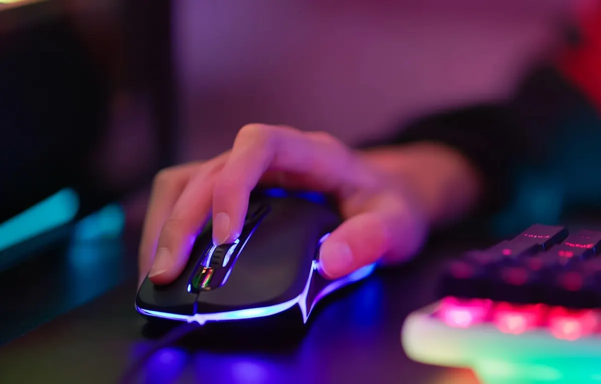 Eine Hand liegt auf einer Gamingmaus neben einem beleuchteten Keyboard.