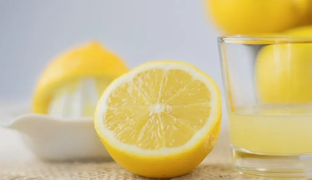 Halbierte Zitrone im Vordergrund neben einem Glas mit Zitronensaft; im Hintergrund eine Zitronenpresse und weitere Zitronen.