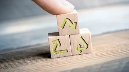 Drei Holzwuerfel mit Recycling Symbol werden zu einem Turm gestapelt