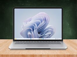 Silberner Laptop mit Windows-Startbildschirm steht auf einem Holztisch.