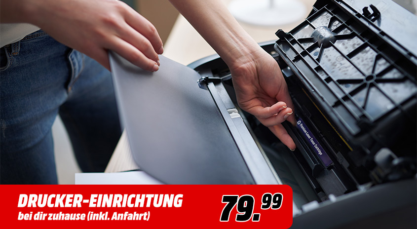 Ein Drucker wird eingerichtet. Eine Hand legt Papier in den Drucker ein, während eine andere Hand eine schwarze Tintenpatrone hält.