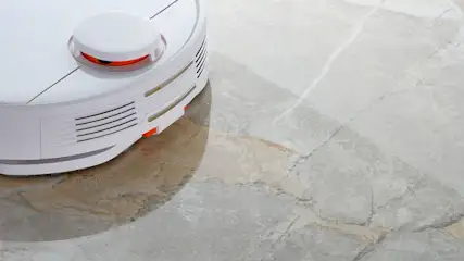 Ein weißer Saugroboter reinigt einen hellen Marmorboden.