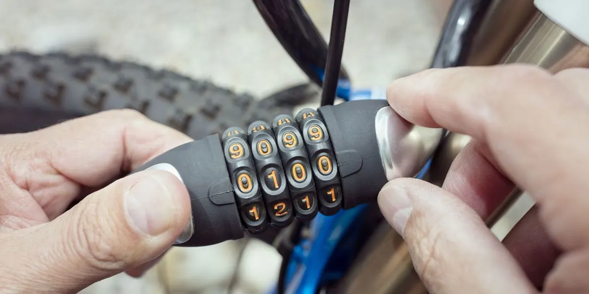 Haende stellen an einem Fahrradschloss mit Zahlencode die Zahlen ein, im Hintergrund ist ein Fahrradreifen zu sehen.