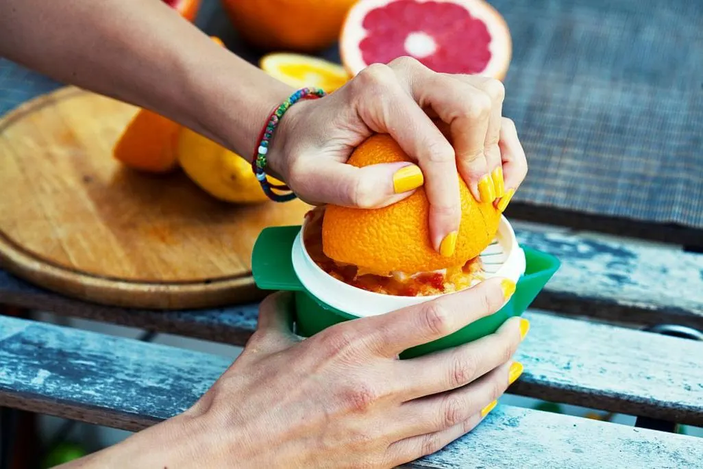 Haende pressen eine Orange mit einer manuellen Zitruspresse auf einem Holztisch