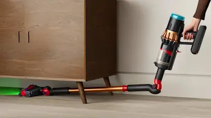 Kabelloser Staubsauger mit flexiblem Rohr, der mühelos Staub unter einem niedrigen Holzschrank entfernt.