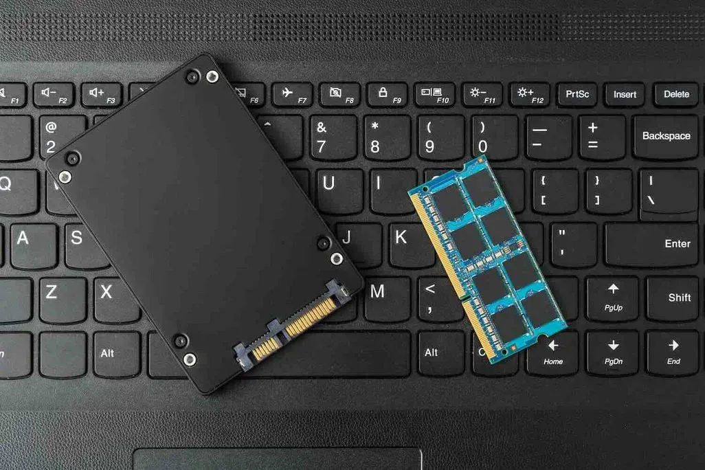 Schwarze SSD und blauer RAM‑Riegel liegen auf der Tastatur eines Laptops – Symbol für Aufrüstung und Leistungssteigerung von Computern.