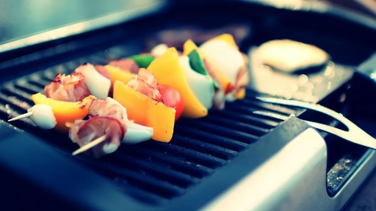 Bunte Gemüsespießchen mit Paprika Zwiebel und Speck werden auf Grill zubereitet.