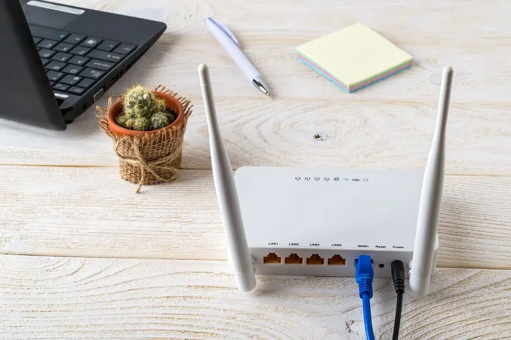 WLAN Router mit zwei Antennen und zwei Kabeln steht auf Schreibtisch neben Laptop