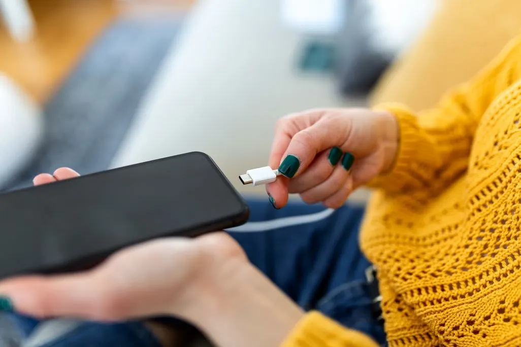 Hand steckt ein USB C Kabel in ein schwarzes Smartphone.