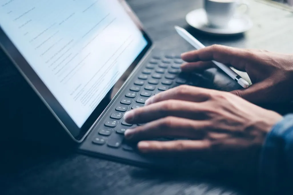 Hände tippen auf Laptop-Tastatur während Textbearbeitung am Bildschirm.