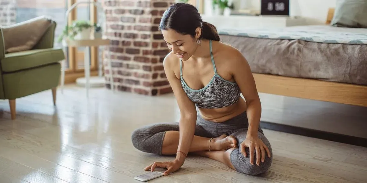 Frau sitzt im Wohnzimmer im schneideritz am Boden und tippt auf einem Handy