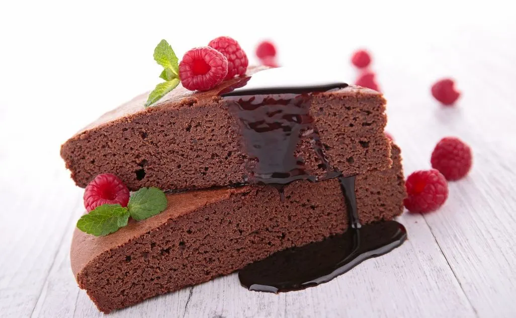 Zwei Stücke Schokoladenkuchen mit Schokosauce und frischen Himbeeren dekoriert.