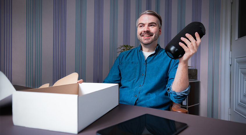 Lächelnder Mann packt Bluetooth Lautsprecher aus einem Karton aus