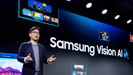 Person steht auf einer Bühne vor einer großen Leinwand mit der Aufschrift Samsung Vision AI und präsentiert.