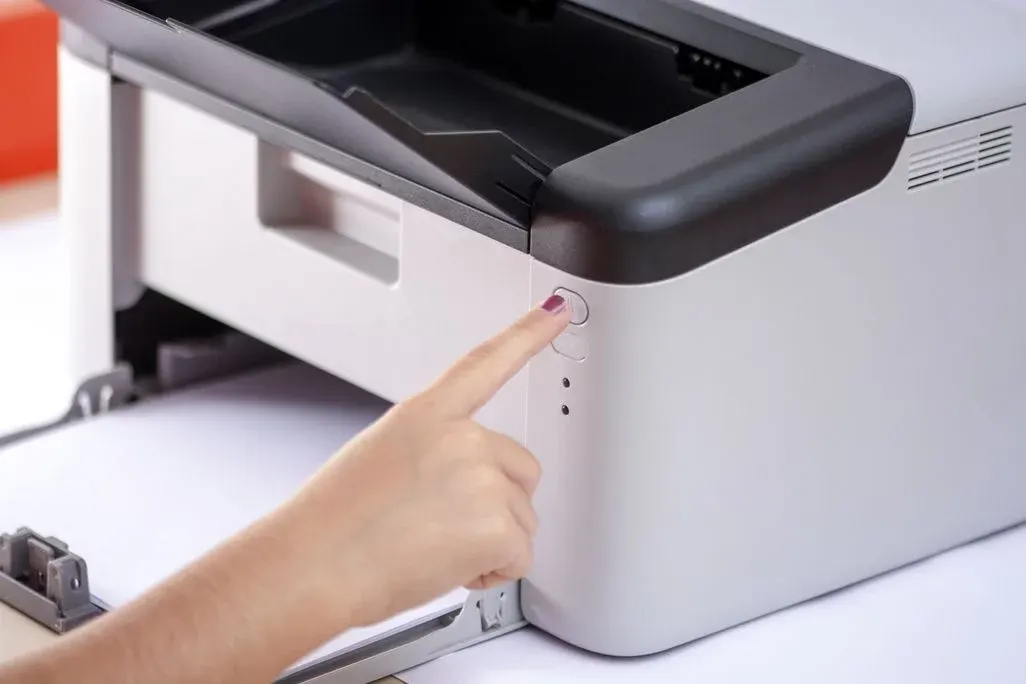 Hand drückt Taste auf weißem Laserdrucker mit offenem Papierfach.