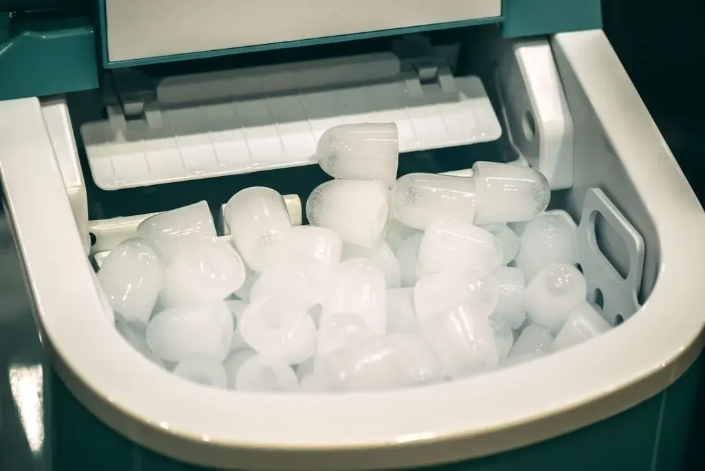 Eismaschine‑Fach mit geformten, hohlen Eiswürfeln im Auffangbehälter, Nahaufnahme.
