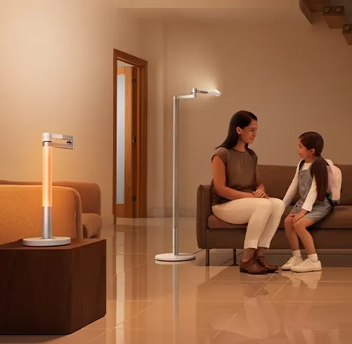 Eine Frau und ein Kind sitzen auf einem braunen Sofa. Eine Stehlampe und eine Tischlampe leuchten im Raum.